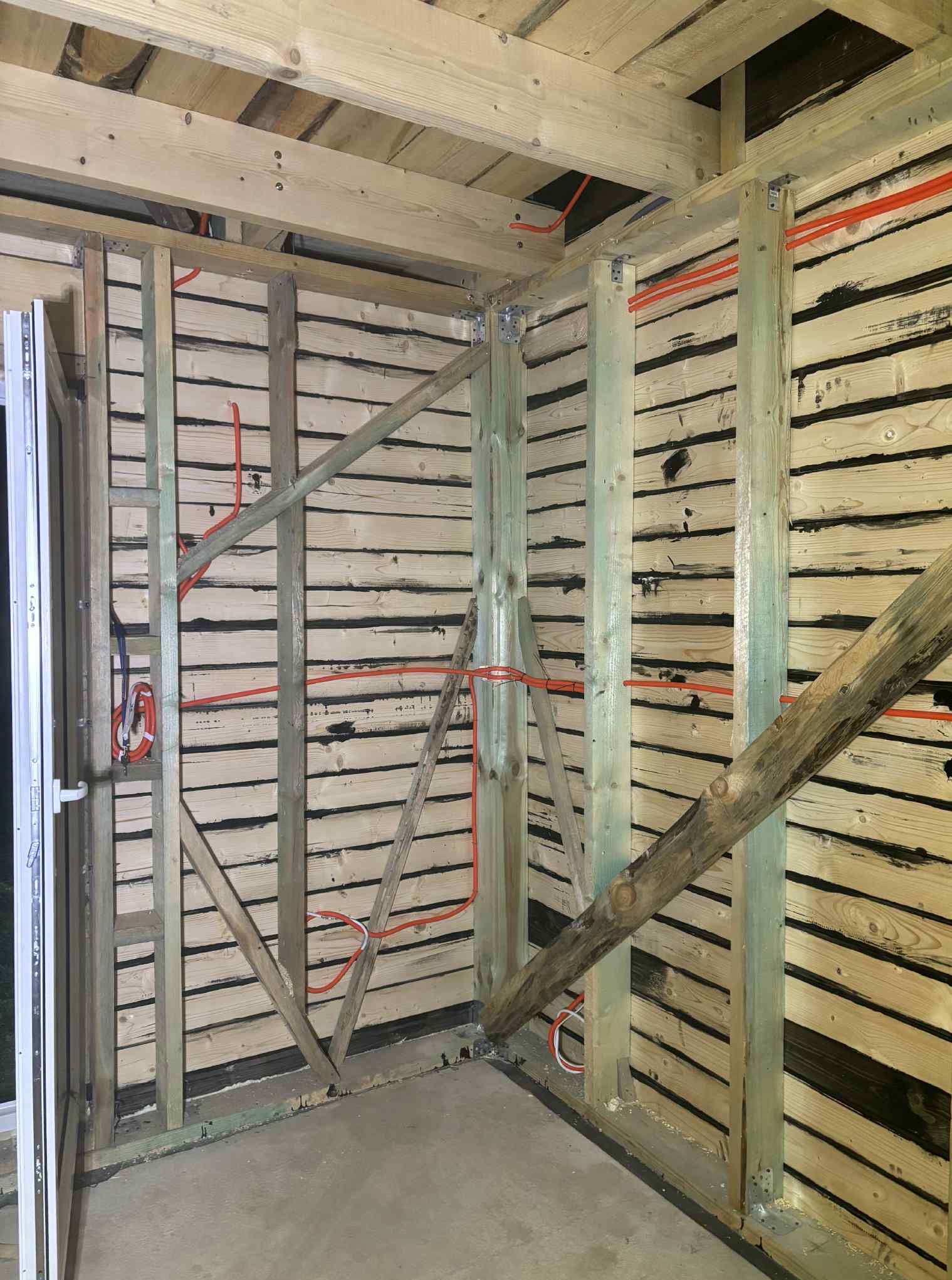 Surowa drewniana konstrukcja ścian z widocznymi przewodami elektrycznymi w pomarańczowej osłonie, świeżo poprowadzonymi wewnątrz budynku.