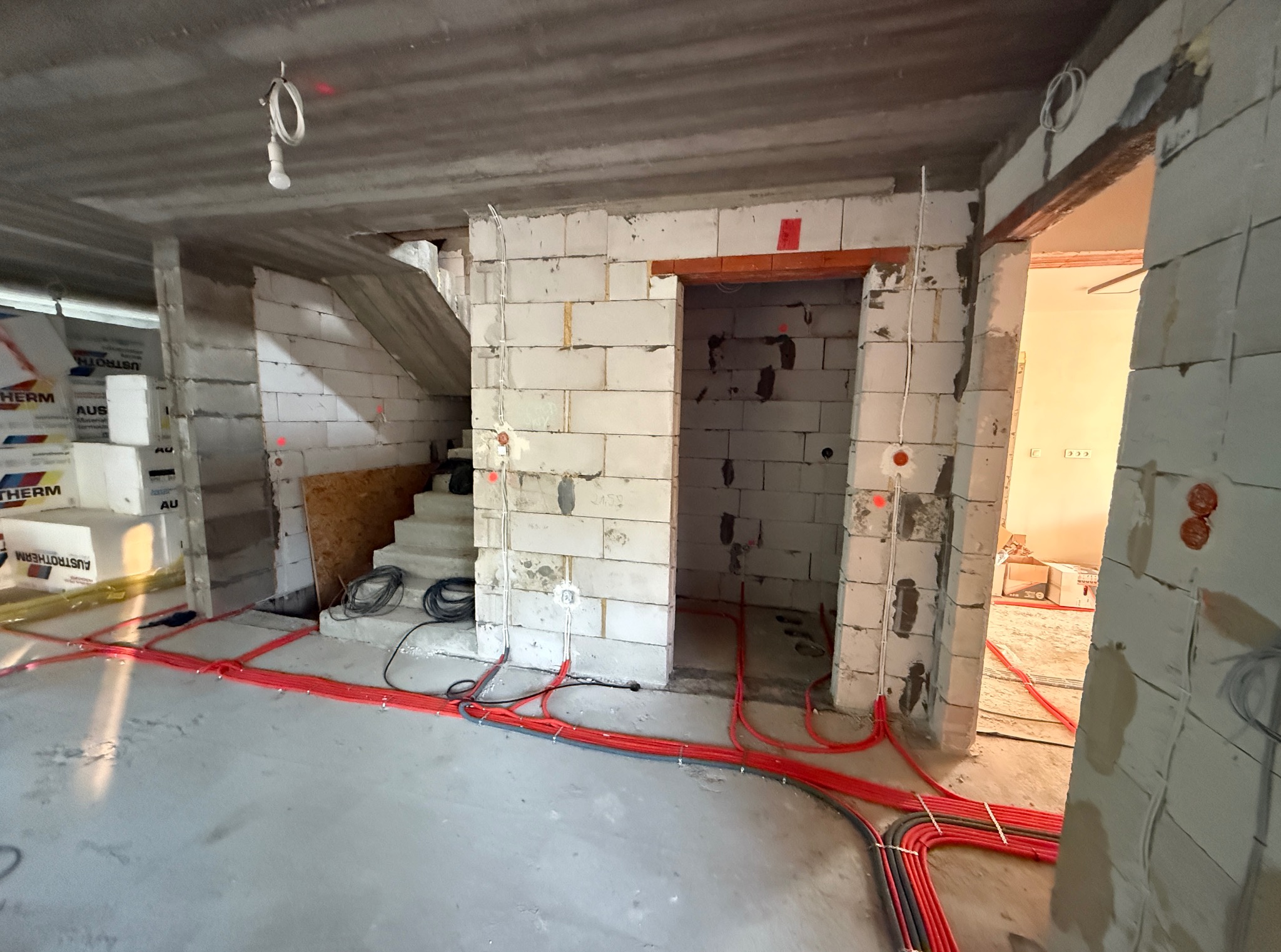 Wnętrze w trakcie budowy z widoczną instalacją elektryczną w peszlach na podłodze, ściany z betonu komórkowego, surowy stan.