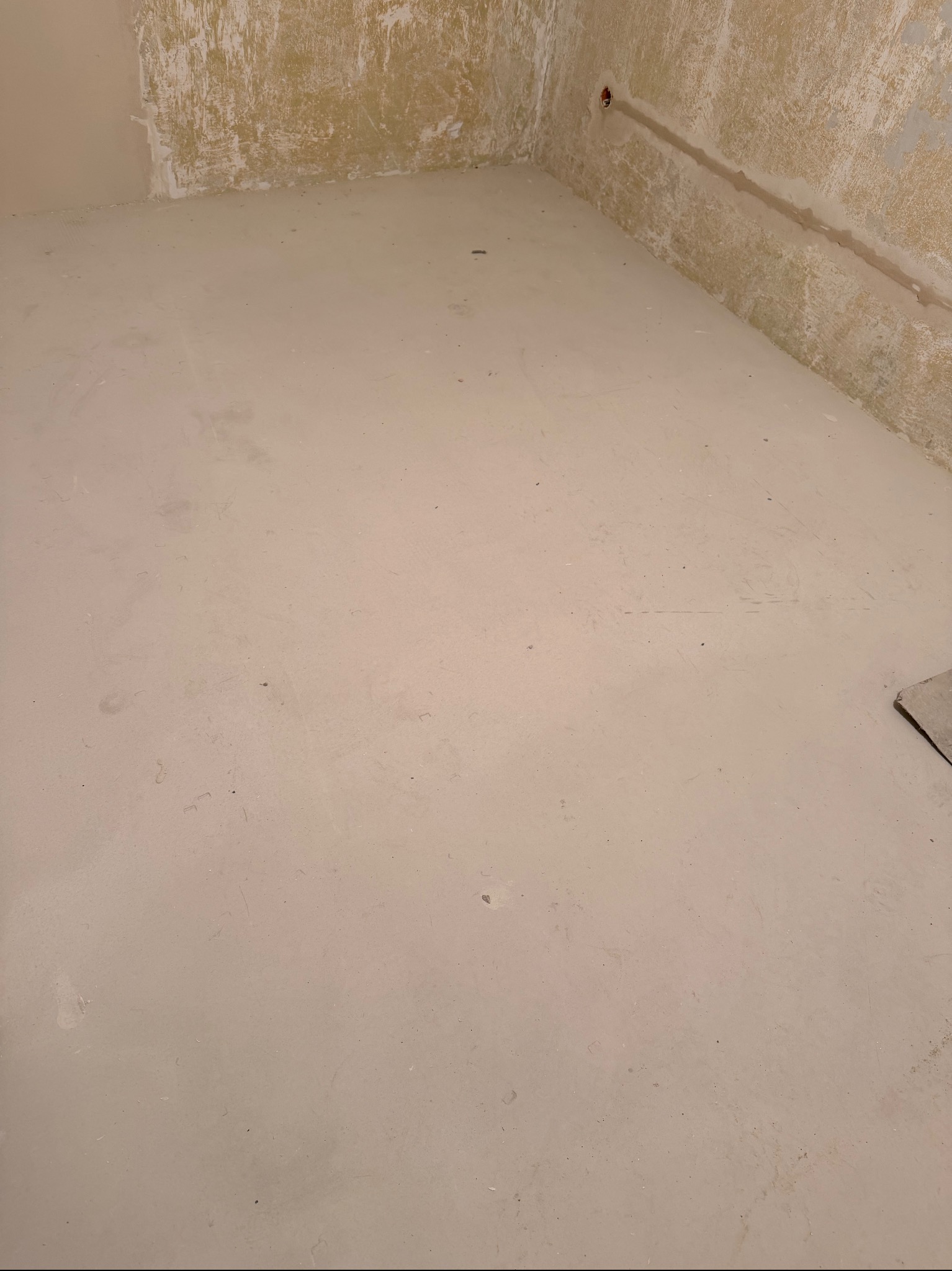 Wyrównana, jasna wylewka podłogowa w pomieszczeniu w Ostrorogu, przygotowana pod dalsze prace wykończeniowe. Ściany częściowo przygotowane do malowania.