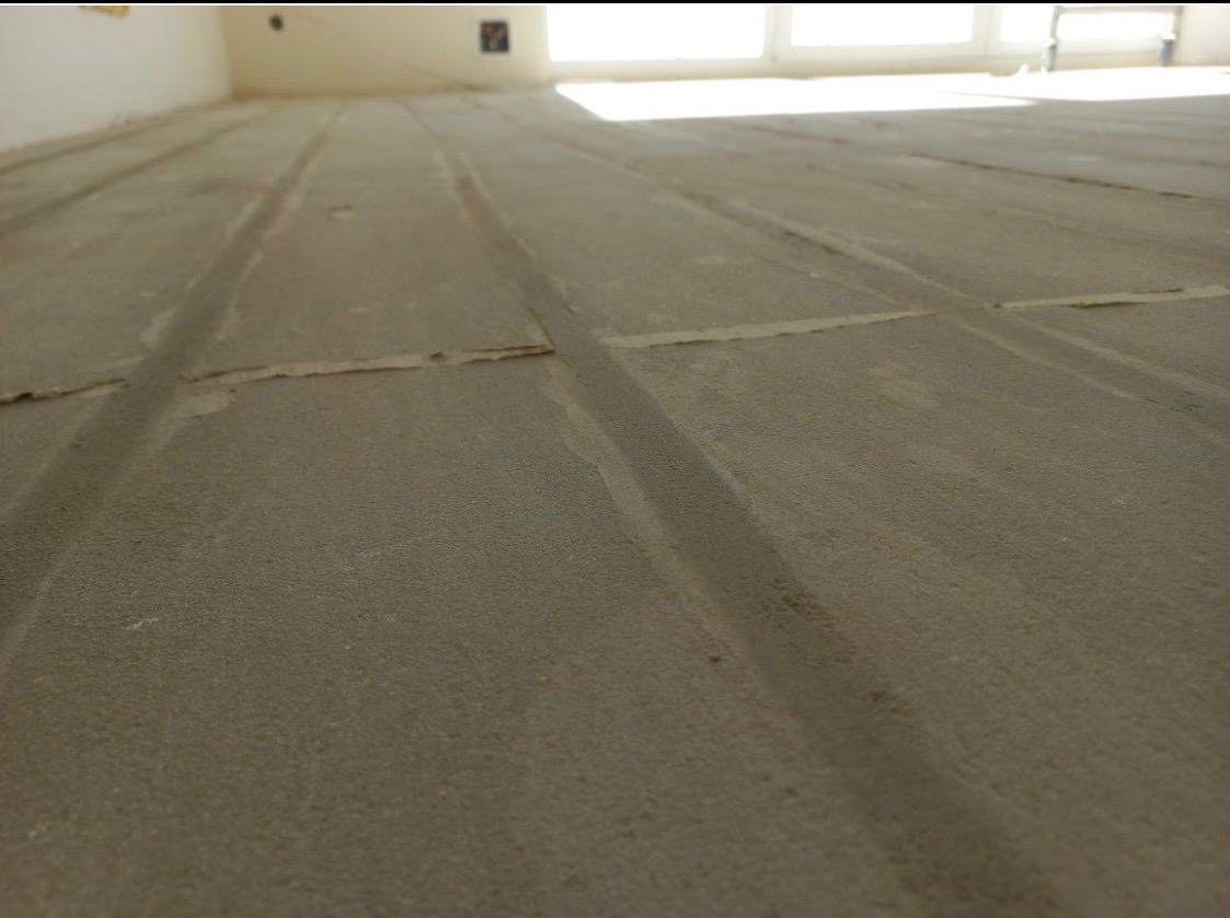 Szare płyty podłogowe z wyżłobieniami pod ogrzewanie podłogowe, widok z niskiej perspektywy, jasne światło z okna w tle.