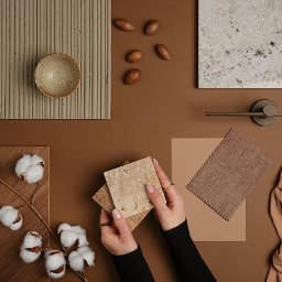 Modern Impact - Paleta barw i materiałów do aranżacji wnętrz w odcieniach brązu, z dłońmi trzymającymi próbki płytek. Widoczne drewno, ceramika, tkanina i element armatury.