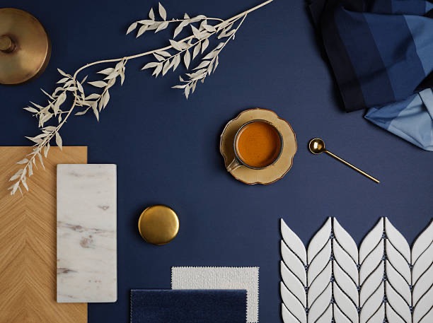 Kompozycja materiałów wykończeniowych w odcieniach granatu i złota: płytki, drewno, marmur, tkaniny, filiżanka kawy i dekoracyjna gałązka. Elegancki moodboard.