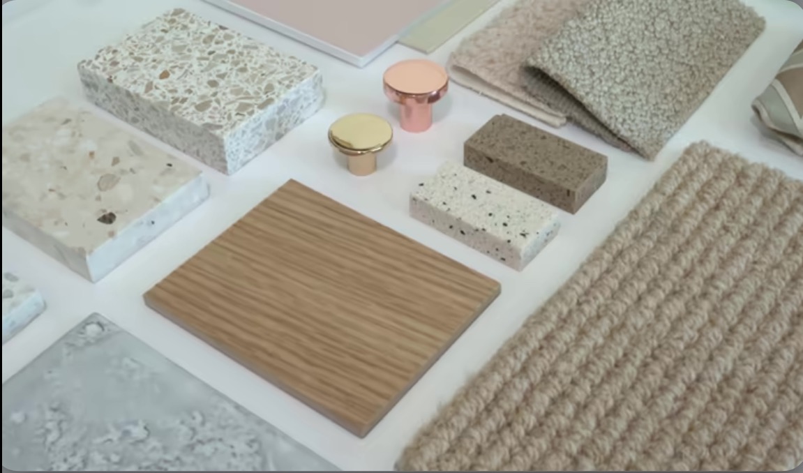 Paleta próbek materiałów wykończeniowych: kamień, drewno, tkaniny i metalowe uchwyty meblowe w neutralnej kolorystyce, prezentowane na białym tle.