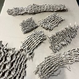 BOX-MASTER - Falista tektura pocięta na paski, ułożona w nieregularne kształty na szarym tle. Materiał wypełniający paczki, widok z góry, oświetlenie studyjne.