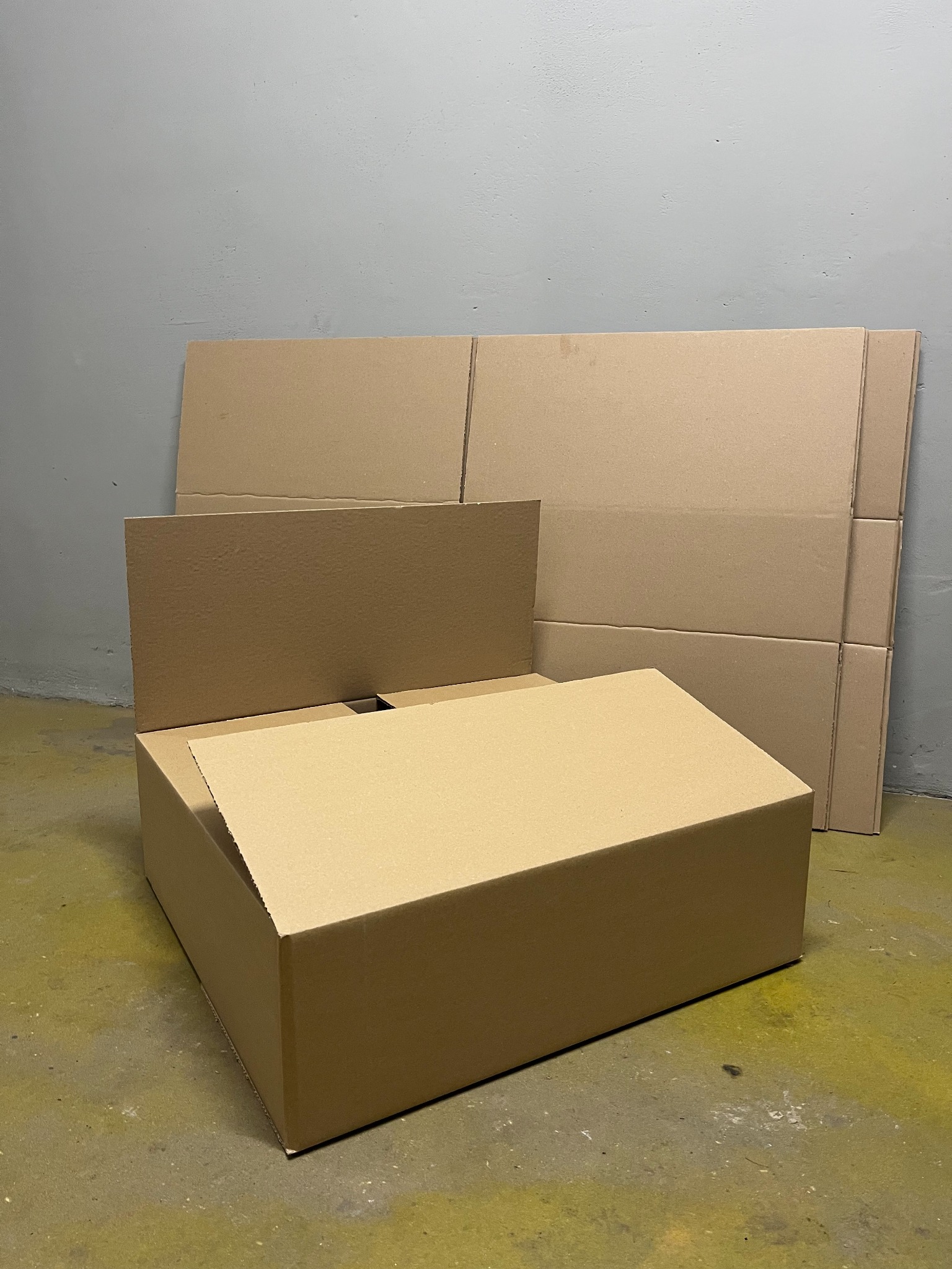 Rozłożone i złożone brązowe kartonowe pudła na szarym tle. Jedno pudełko złożone, inne w płaskich arkuszach, gotowe do użycia. Widok z bliska.