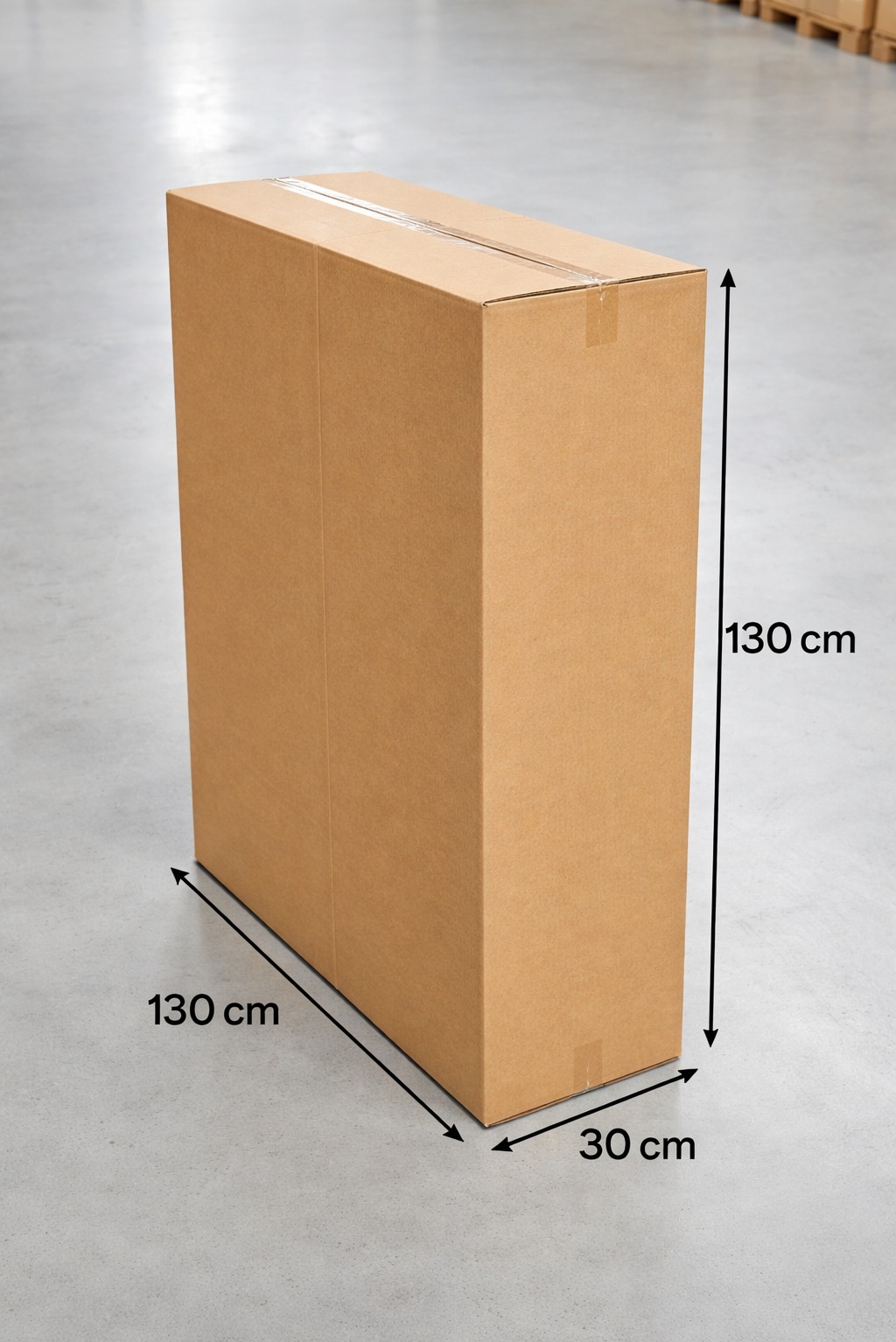 Wysoki, prostokątny karton z taśmą, o wymiarach 130x130x30 cm, stoi na szarym betonowym podłożu. W tle widoczne fragmenty drewnianych palet.