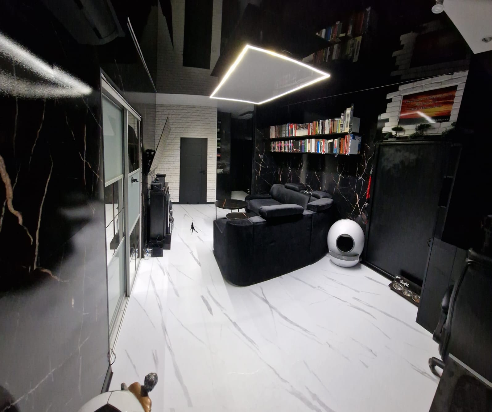 Nowoczesny salon w czerni i bieli z marmurowymi akcentami. Biała podłoga z szarymi żyłami, czarne ściany z marmurowym wzorem, designerska lampa sufitowa i minimalistyczne meble.