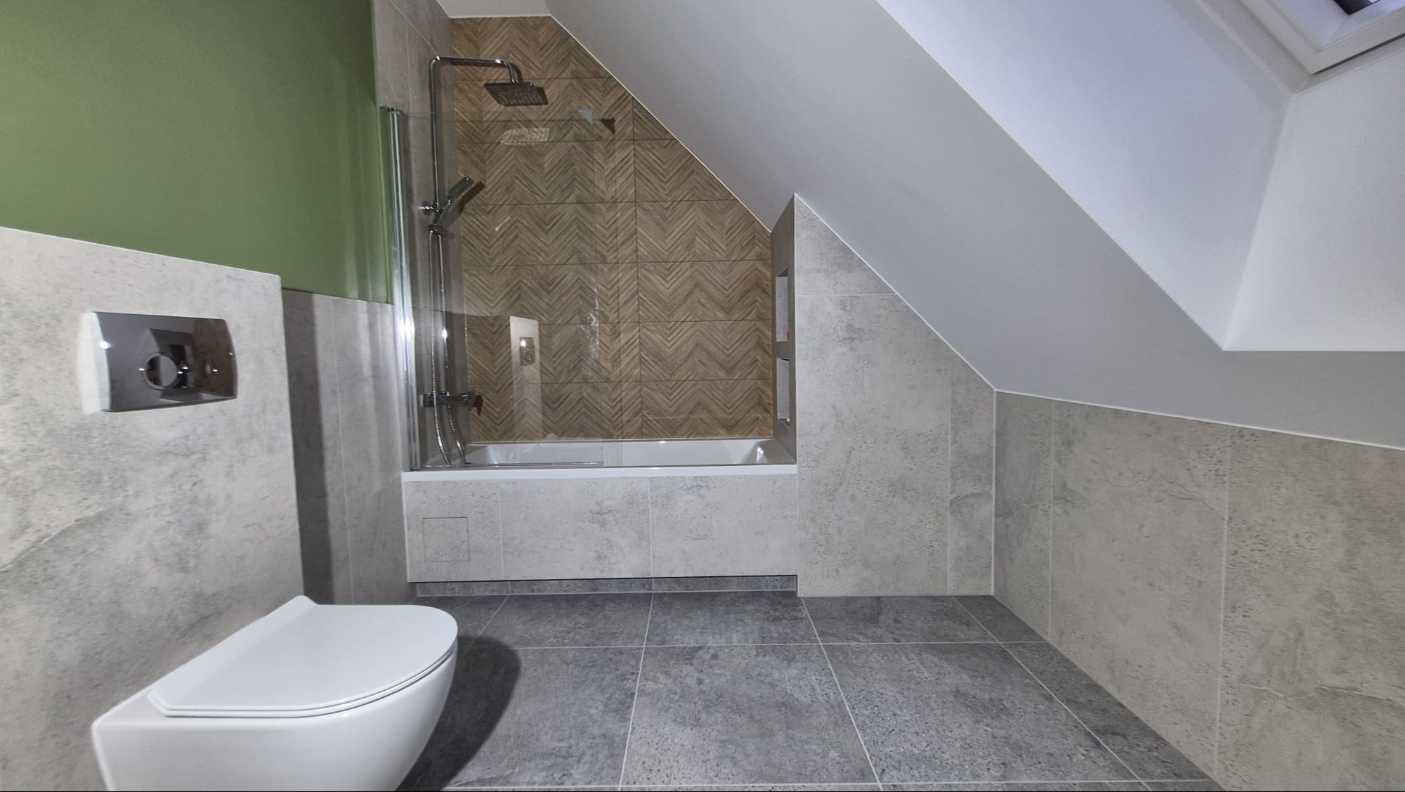 Nowoczesna łazienka na poddaszu z szarą glazurą, białą armaturą i akcentem zielonej ściany. Uwagę przykuwają płytki imitujące drewno ułożone w jodełkę nad wanną.