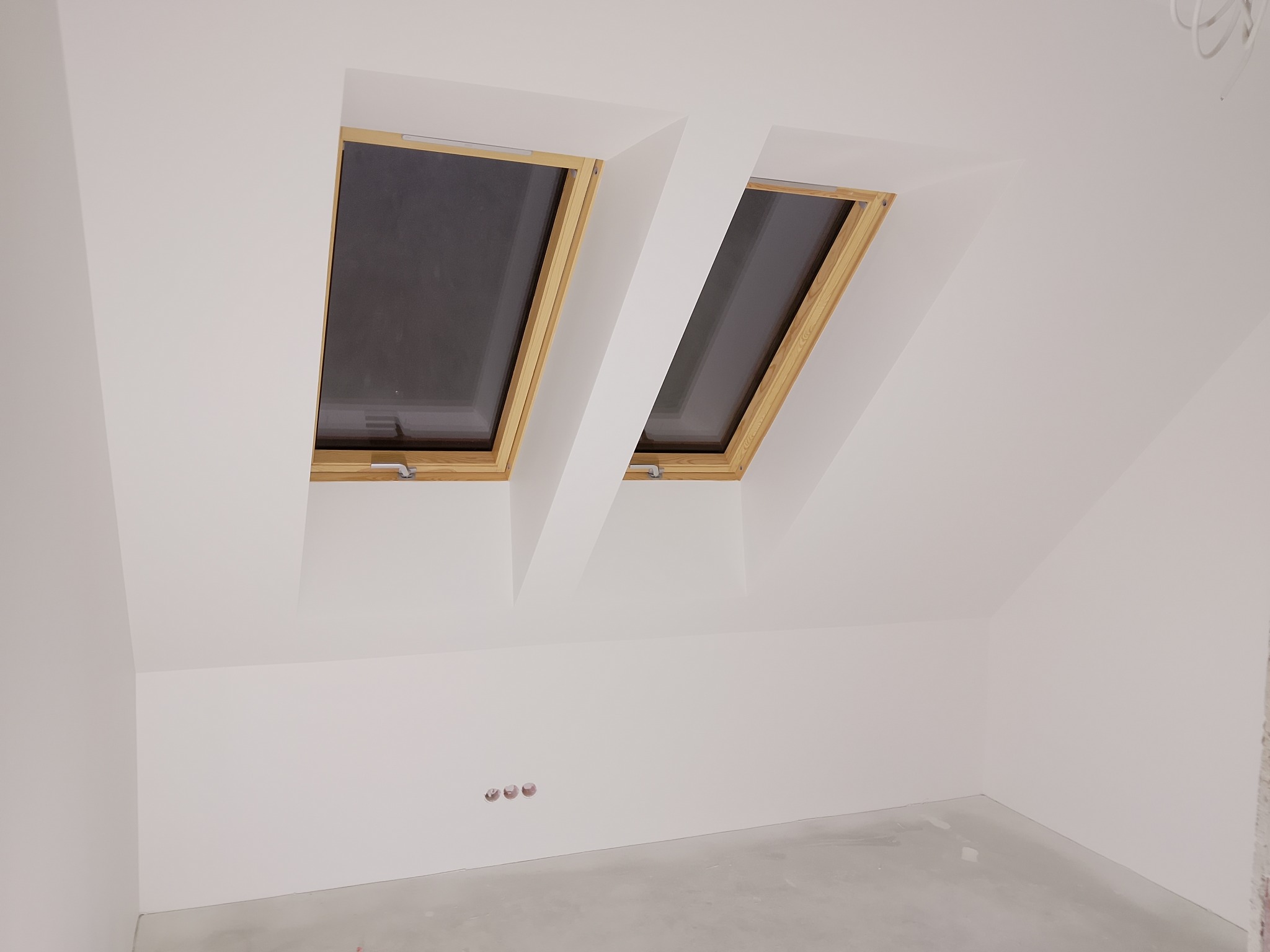 Białe poddasze z dwoma oknami dachowymi w drewnianych ramach. Świeżo pomalowane ściany i gładka podłoga w Limanowej. Widoczne gniazdka elektryczne.