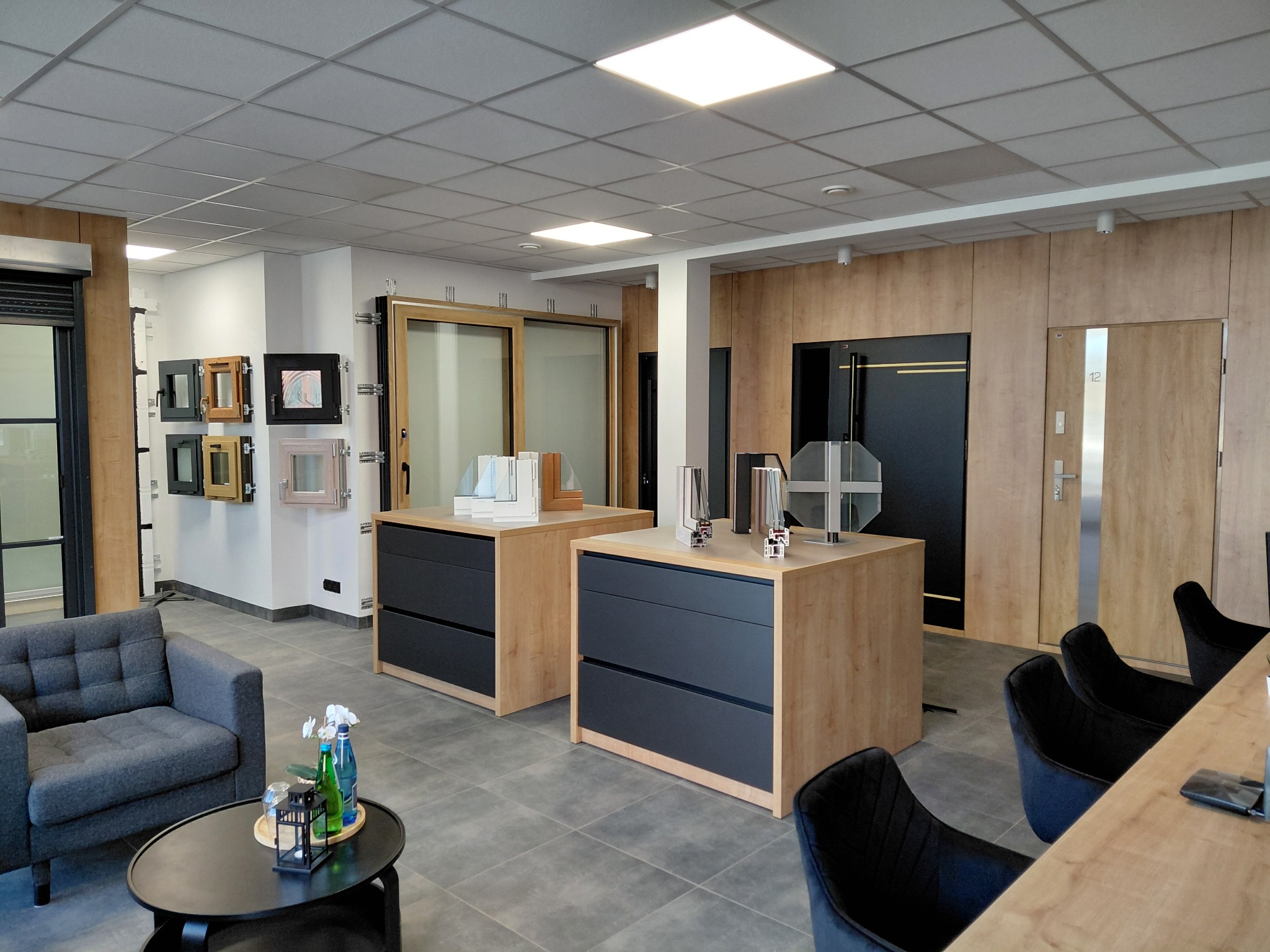 Salon z ekspozycją okien, drzwi i rolet. Widoczne ramy okienne, drzwi wewnętrzne, rolety oraz meble ekspozycyjne w nowoczesnym wnętrzu.