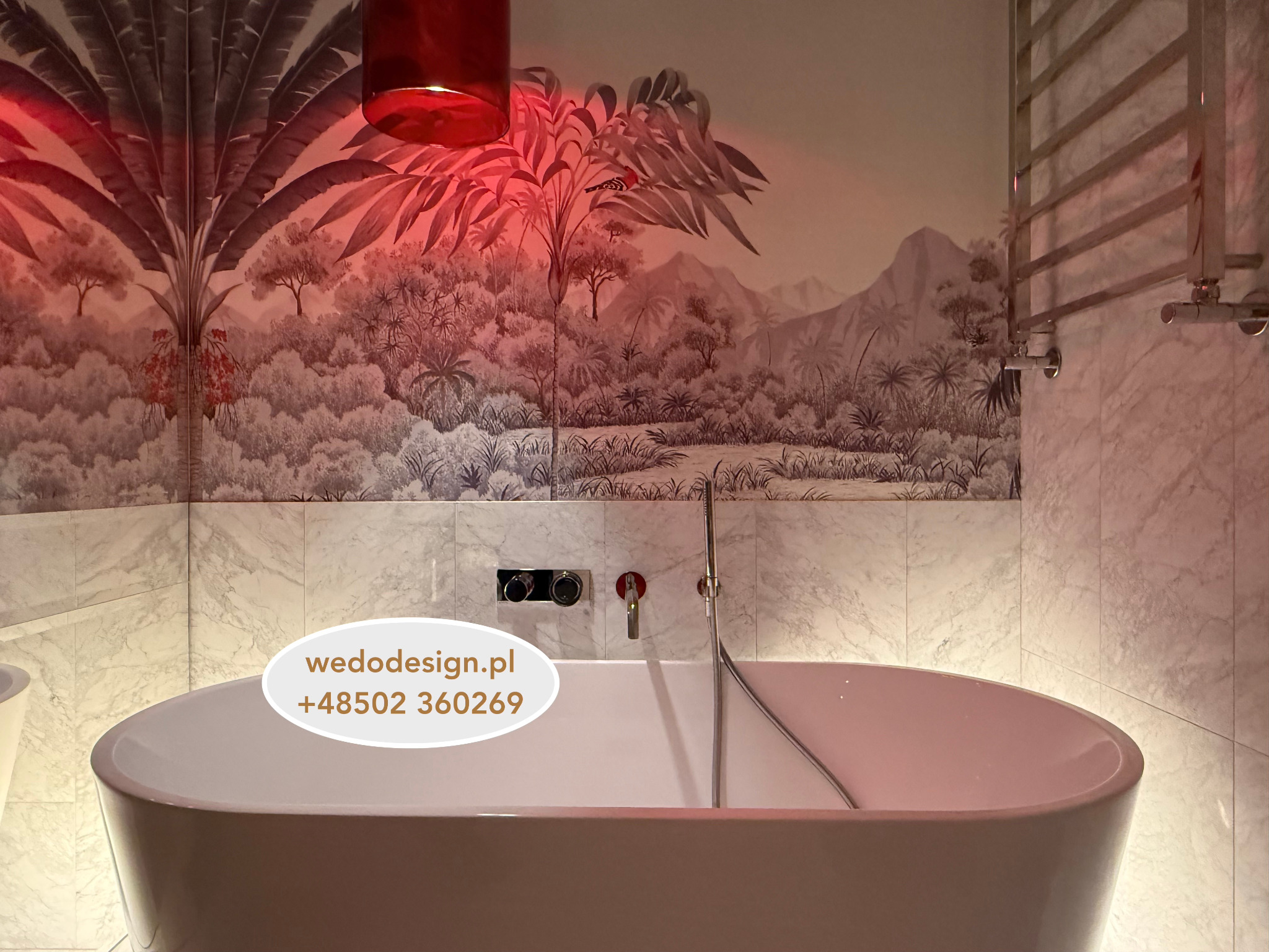 Nowoczesna łazienka z wolnostojącą wanną, marmurowymi płytkami i tapetą w tropikalny wzór, oświetlona czerwonym światłem. Bateria ścienna w kolorze złota.