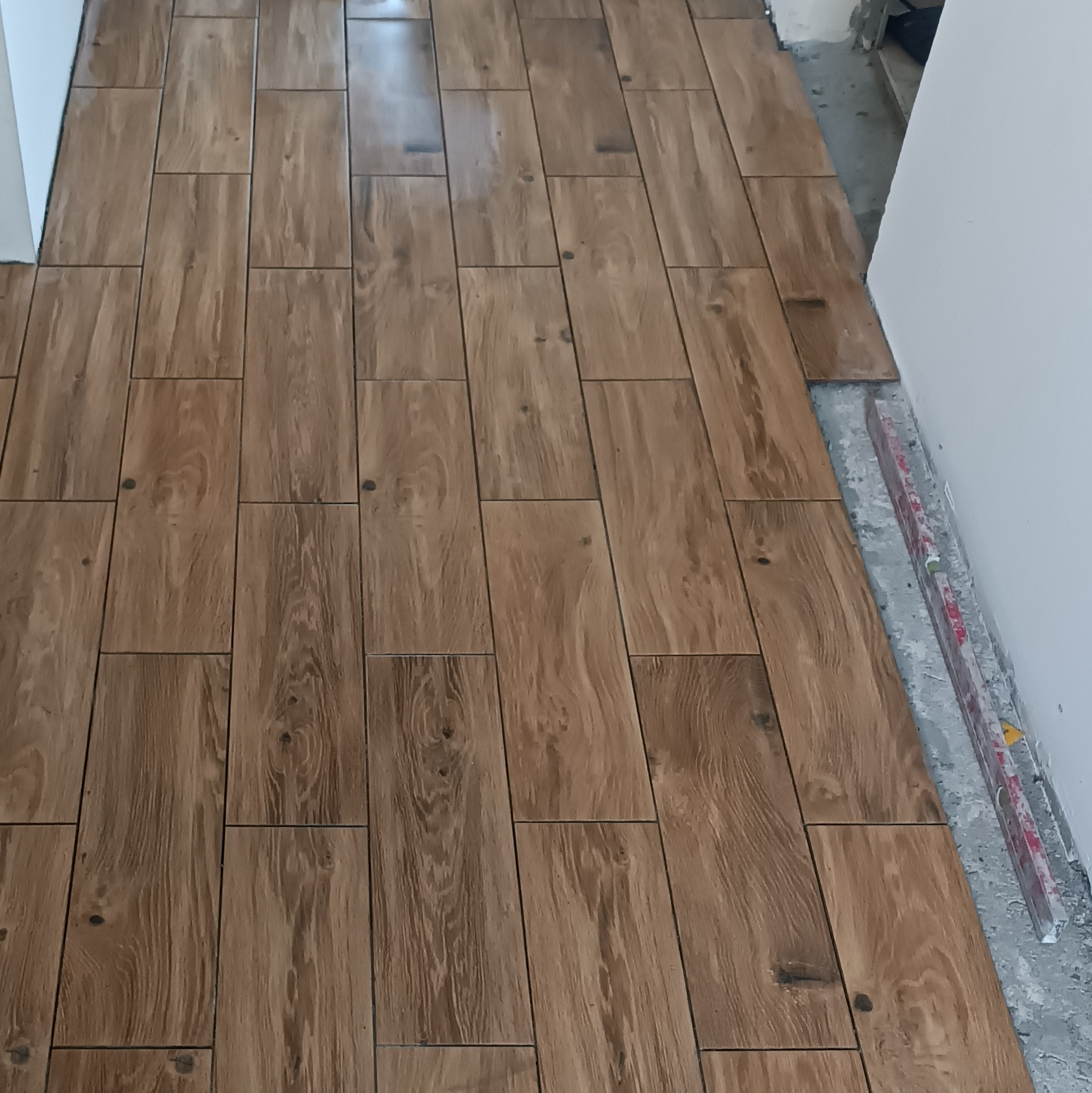 Układanie podłogi z płytek imitujących drewno w Karsko. Widoczny fragment podłogi w trakcie prac wykończeniowych, z poziomnicą przy ścianie.