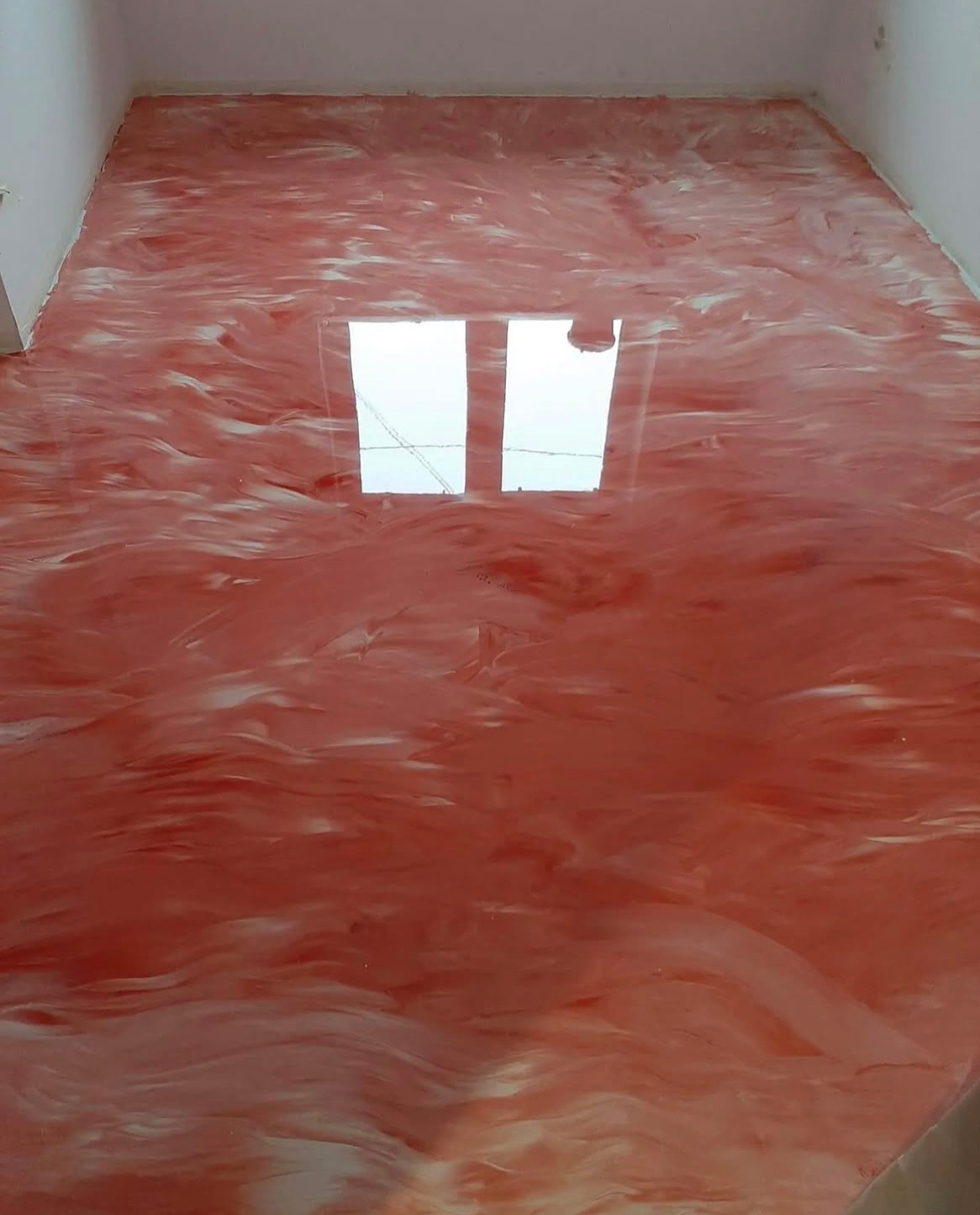 Błyszcząca, czerwono-biała posadzka w pokoju z odbiciem okna, tworząca unikalny, marmurkowy wzór na całej powierzchni podłogi.