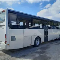 Biały autobus Crossway 12M z przyciemnianymi szybami, zaparkowany na zewnątrz, widok z tyłu i boku, błękitne niebo z chmurami w tle.