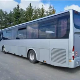 Srebrny autobus Crossway na zewnątrz, widok z tyłu i boku, z zielonymi drzewami w tle i numerem rejestracyjnym widocznym na tablicy.
