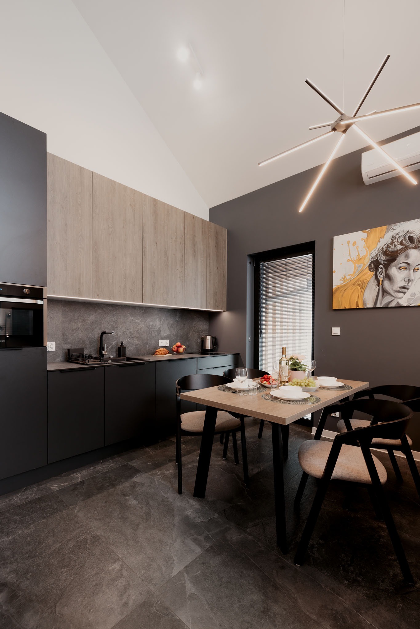 Nowoczesna kuchnia w odcieniach szarości z drewnianymi akcentami. Minimalistyczny design, oświetlenie LED i dekoracyjny obraz tworzą spójną całość.