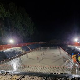 Energetyka i Budownictwo Inwestycje Sp. z o.o. - Nocne betonowanie fundamentów zbrojonych na budowie. Widoczni pracownicy w odblaskowych kamizelkach i kaskach, pompa do betonu, oświetlenie budowlane.