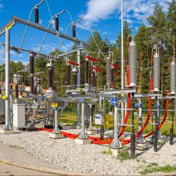 Energetyka i Budownictwo Inwestycje Sp. z o.o. - Rozległa stacja transformatorowa z licznymi elementami elektrycznymi na tle lasu i błękitnego nieba. Widoczne transformatory, izolatory i kable.