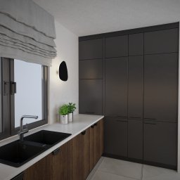 PauLine Concept Paulina Oszczyk - Minimalistyczna kuchnia z ciemnymi szafkami, drewnianymi frontami i czarnym zlewem przy oknie. Roślina w srebrnych doniczkach dodaje akcentu.