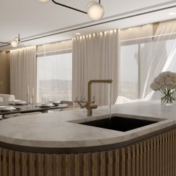 PauLine Concept Paulina Oszczyk - Ekskluzywna kuchnia z wyspą o marmurowym blacie i dekoracyjnym wykończeniu. W tle stół z zastawą i widok na miasto przez okno z delikatnymi zasłonami.