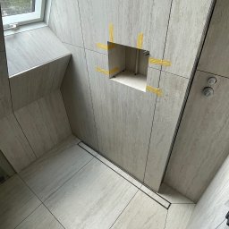 Mateusz Leśnikowski - Wykończona łazienka z beżowymi płytkami imitującymi kamień. Widoczny odpływ liniowy, okno dachowe i otwór na baterię zabezpieczony taśmą. Minimalistyczny design.