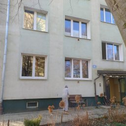 Przedstawiciel handlowy firmy Drutex ,Eko okna,i gdanskiej fabryki okien - Budynek z oknami PCV, widok z zewnątrz. Na pierwszym planie starszy mężczyzna. W oknach odbija się krajobraz. Białe ramy okienne kontrastują z elewacją.