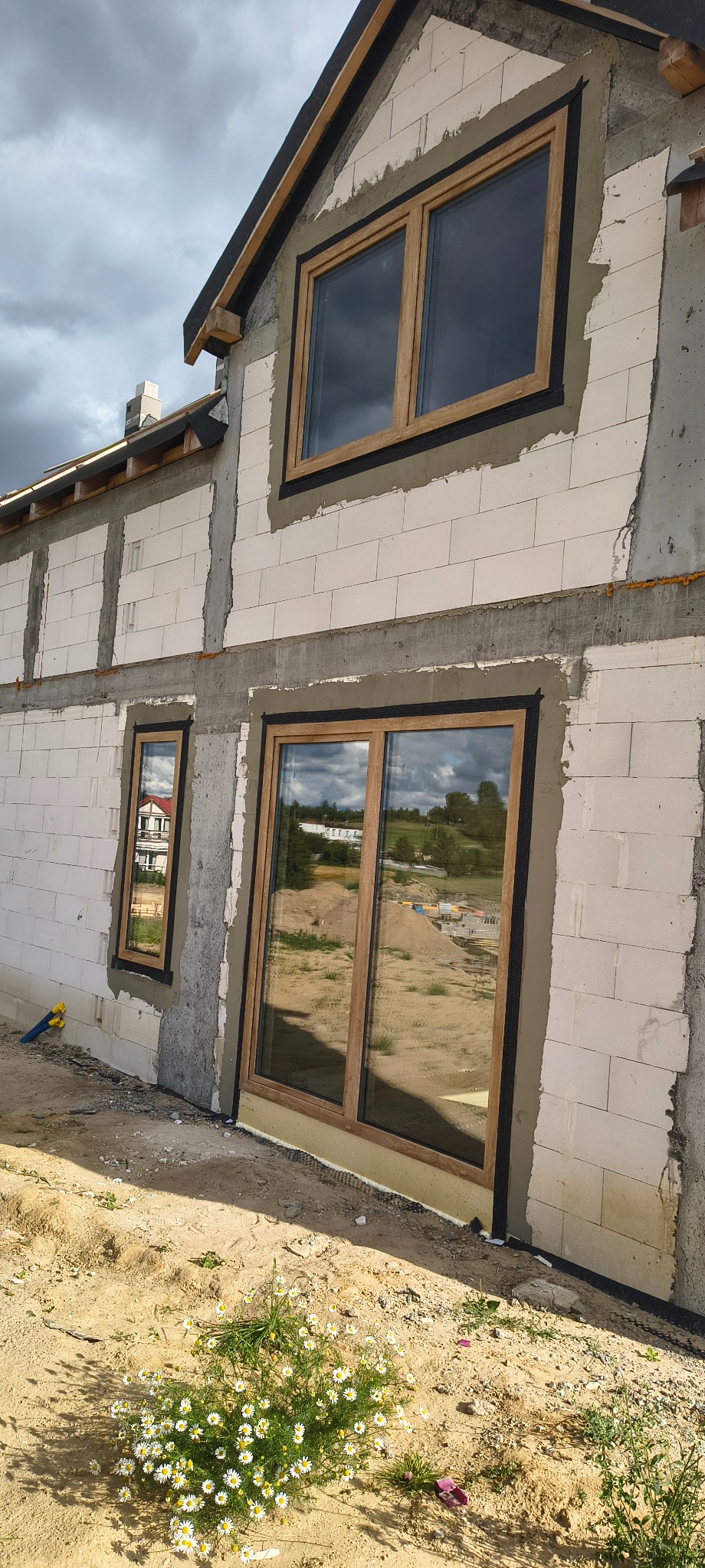 Montaż okien z drewnianą ramą w surowym budynku z betonu komórkowego. Widoczne ocieplenie i przygotowanie do dalszych prac wykończeniowych.