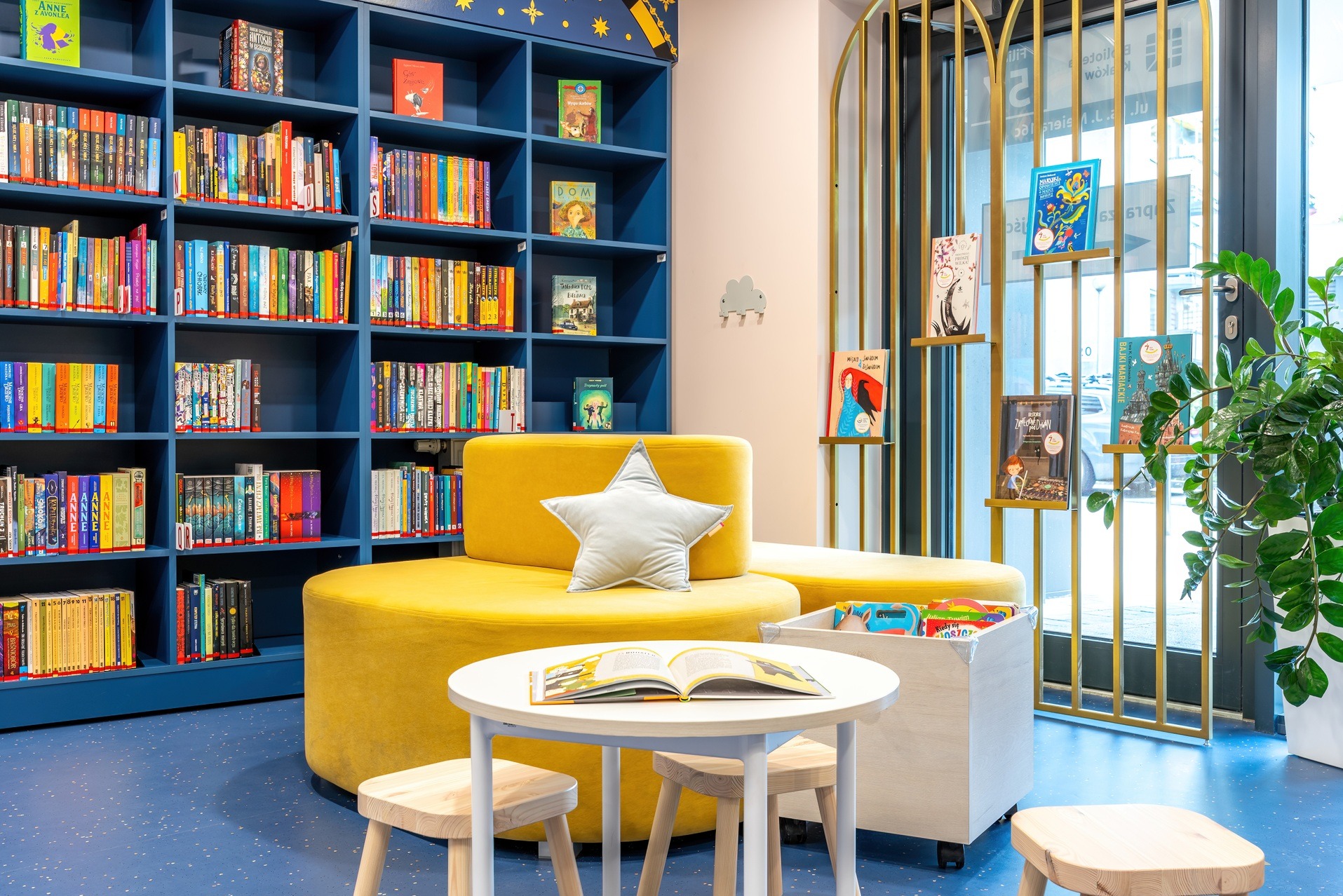 Aranżacja biura w Krakowie: regał z książkami, żółte siedziska i stolik w pokoju dziecięcym. Nowoczesny design biblioteki z elementami dekoracyjnymi.