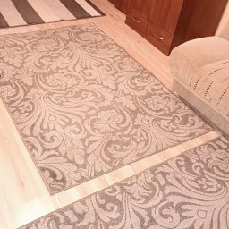 Global Cleaning - Dywan z beżowym wzorem, widok z góry po praniu chemicznym. W tle szafa z ciemnego drewna i fragment sofy.