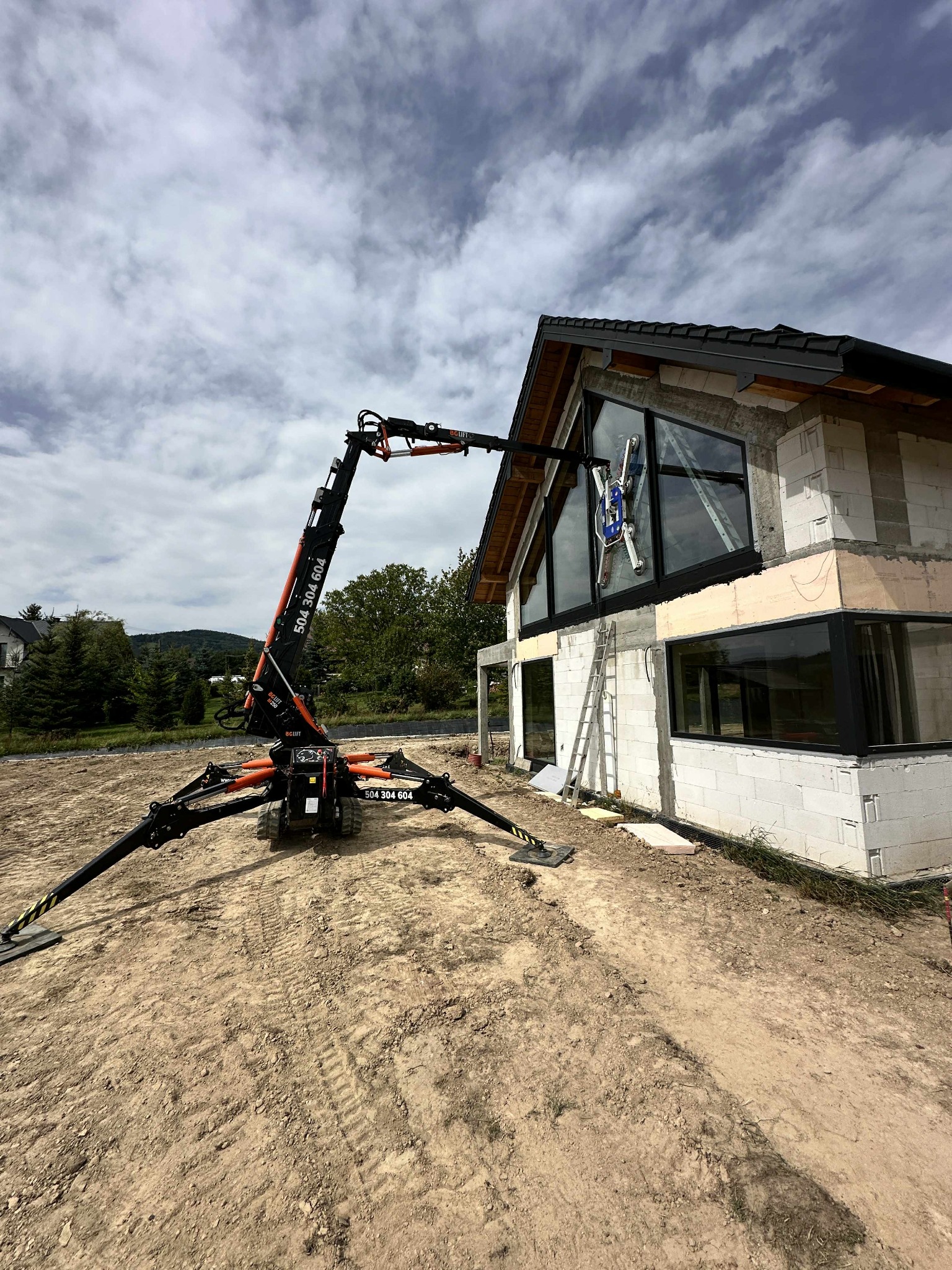 Montaż okien panoramicznych w surowym budynku jednorodzinnym za pomocą specjalistycznego dźwigu z przyssawkami. Widok z dołu na budowę.