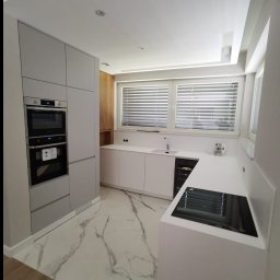 Reda meble - Nowoczesna kuchnia z szarymi szafkami i białym blatem, płyta indukcyjna, marmurowa podłoga, okno z żaluzjami, minimalistyczny design, oświetlenie punktowe.