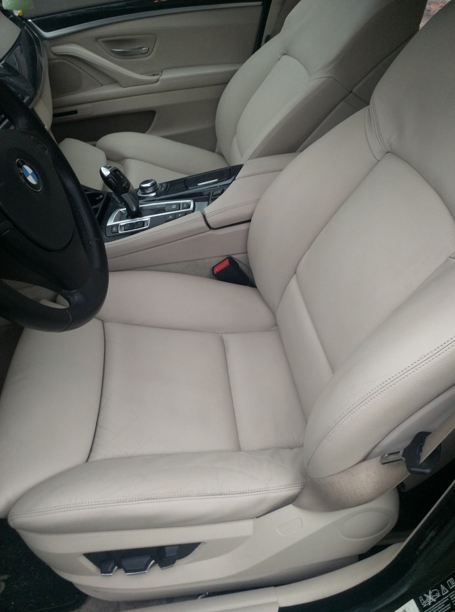 Jasne, skórzane fotele w samochodzie BMW, widoczne z perspektywy kierowcy, z czarną kierownicą po lewej. Detale wnętrza premium.