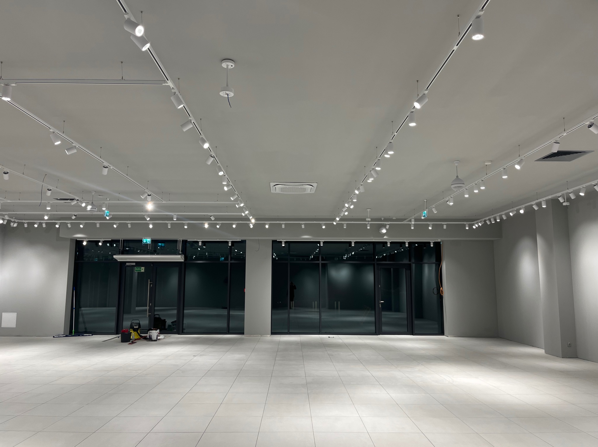 Wnętrze po sprzątaniu w Kadłubska Wola: jasna podłoga, ściany i sufit z oświetleniem. Widoczne narzędzia do sprzątania przy wejściu, duże okna.