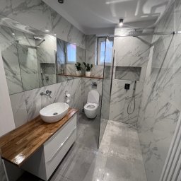 Jacek nazurek - Nowoczesna łazienka z marmurowymi płytkami, drewnianym blatem pod umywalką i szklaną kabiną prysznicową typu walk-in. Minimalistyczny design i eleganckie wykończenie.