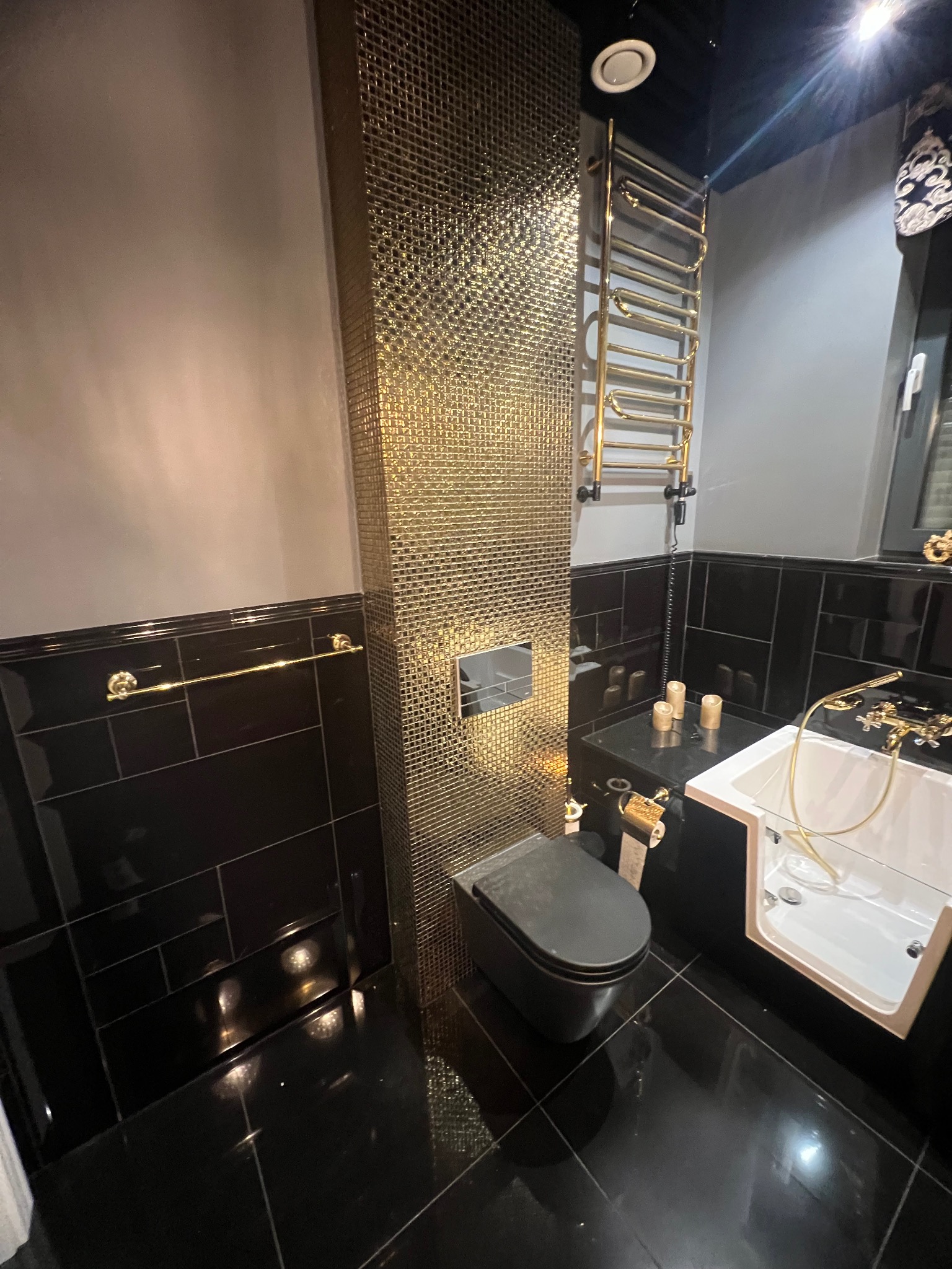 Luksusowa łazienka: czarne płytki, złote akcenty, mozaika, designerska toaleta i grzejnik. Nowoczesny wystrój, eleganckie wykończenie.