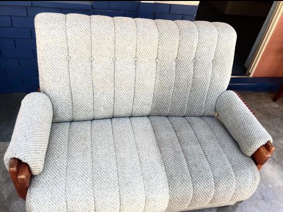 Dwuosobowa kanapa z jasną tapicerką i drewnianymi podłokietnikami, po czyszczeniu. Usługa wykonana w Tychach. Widoczne detale tapicerki i odświeżony wygląd.