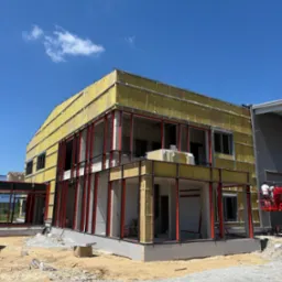 Budynek w trakcie ocieplania we Wrocławiu, widoczne żółte płyty izolacyjne na elewacji i stalowa konstrukcja. Etap prac przed wykończeniem.