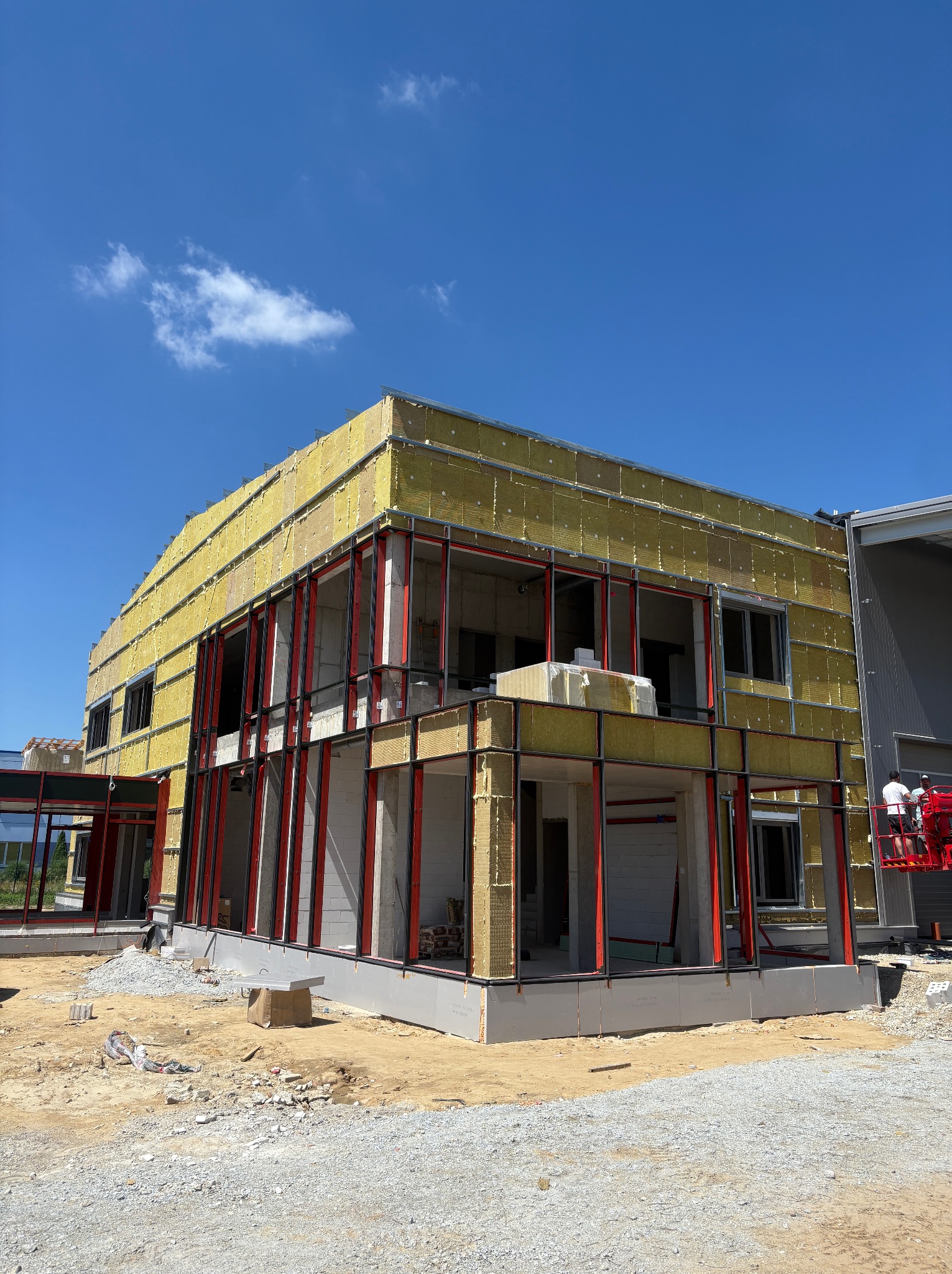 Budynek w trakcie ocieplania we Wrocławiu, widoczne żółte płyty izolacyjne na elewacji i stalowa konstrukcja. Etap prac przed wykończeniem.