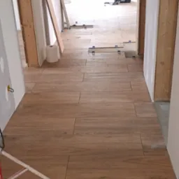 Układanie podłogi z płytek imitujących drewno w korytarzu. Widoczne krzyżyki dystansowe, narzędzia w tle i przygotowane ściany. Wnętrze w trakcie wykończenia.