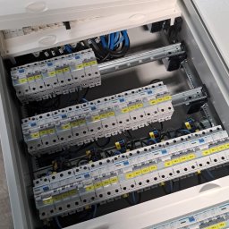 Damian Ławniczek-Wertepny - Rozdzielnica elektryczna z zainstalowanymi bezpiecznikami i okablowaniem, widok z góry, oświetlenie dzienne, etykiety na bezpiecznikach.