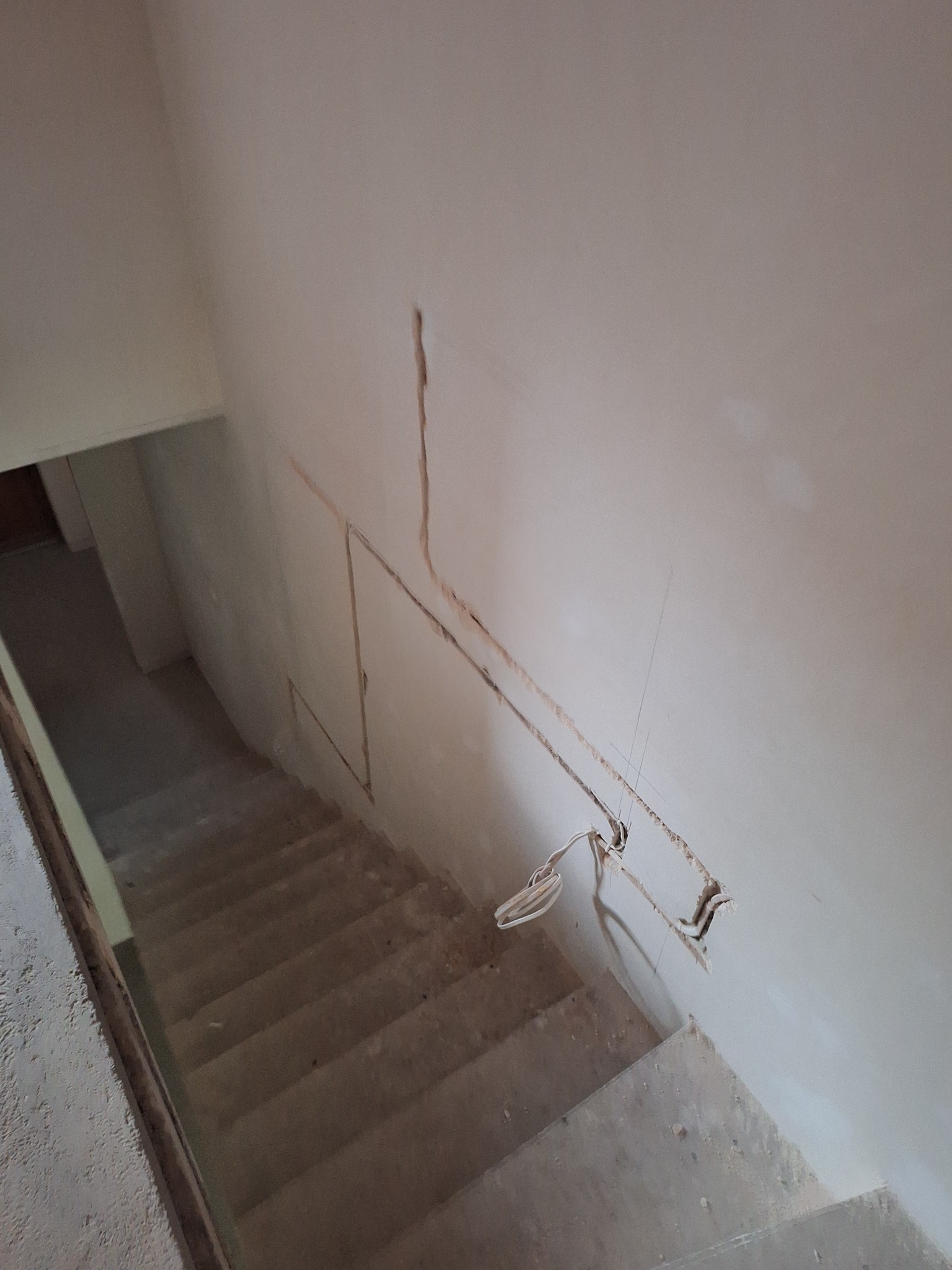 Kable elektryczne wystające ze ściany nad schodami w trakcie remontu. Widoczne bruzdy w ścianie przygotowane pod instalację. Surowy stan wykończenia.