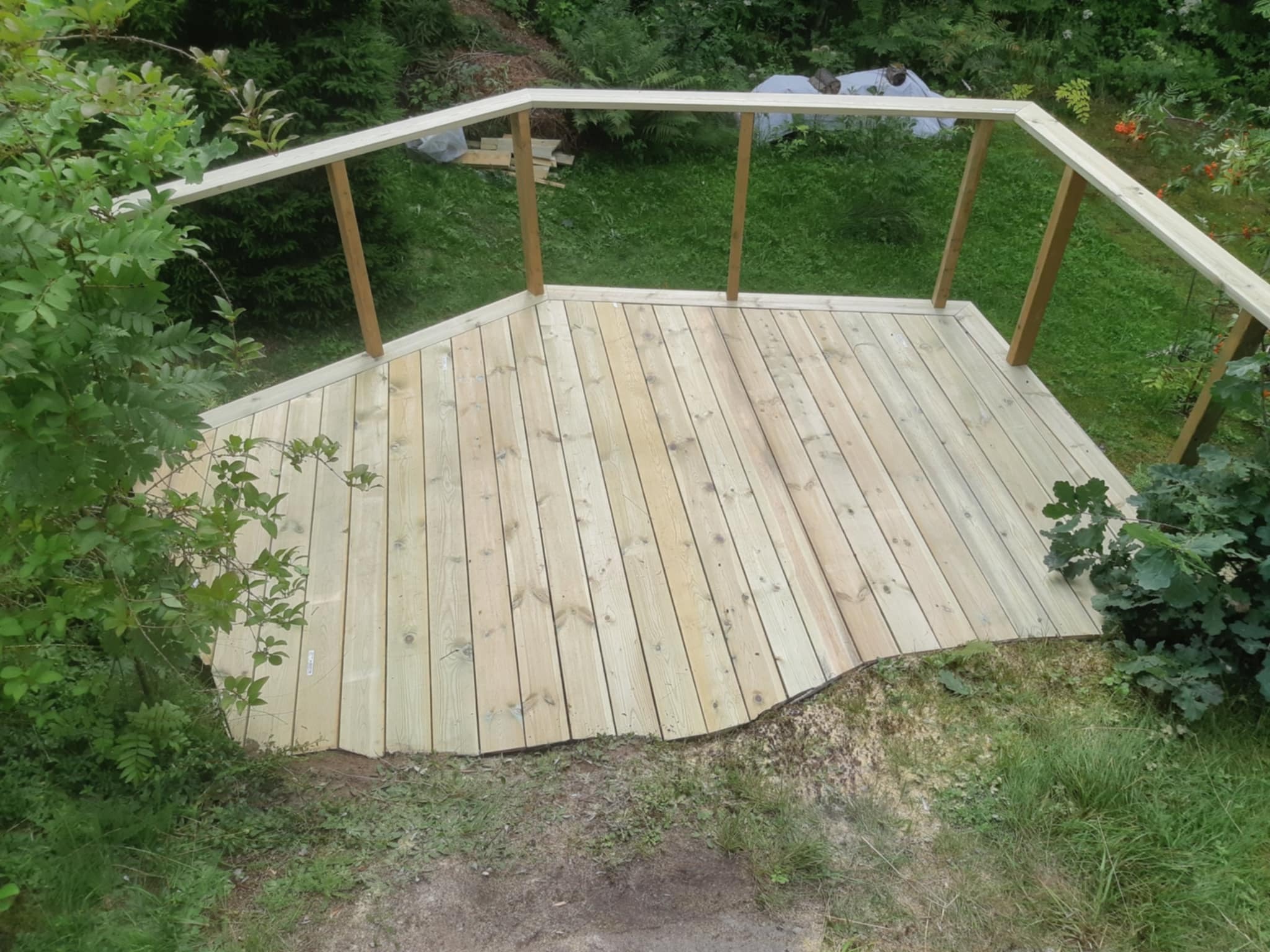 Nowy drewniany taras z balustradą w ogrodzie, świeżo po montażu. Naturalne oświetlenie, widok z góry.