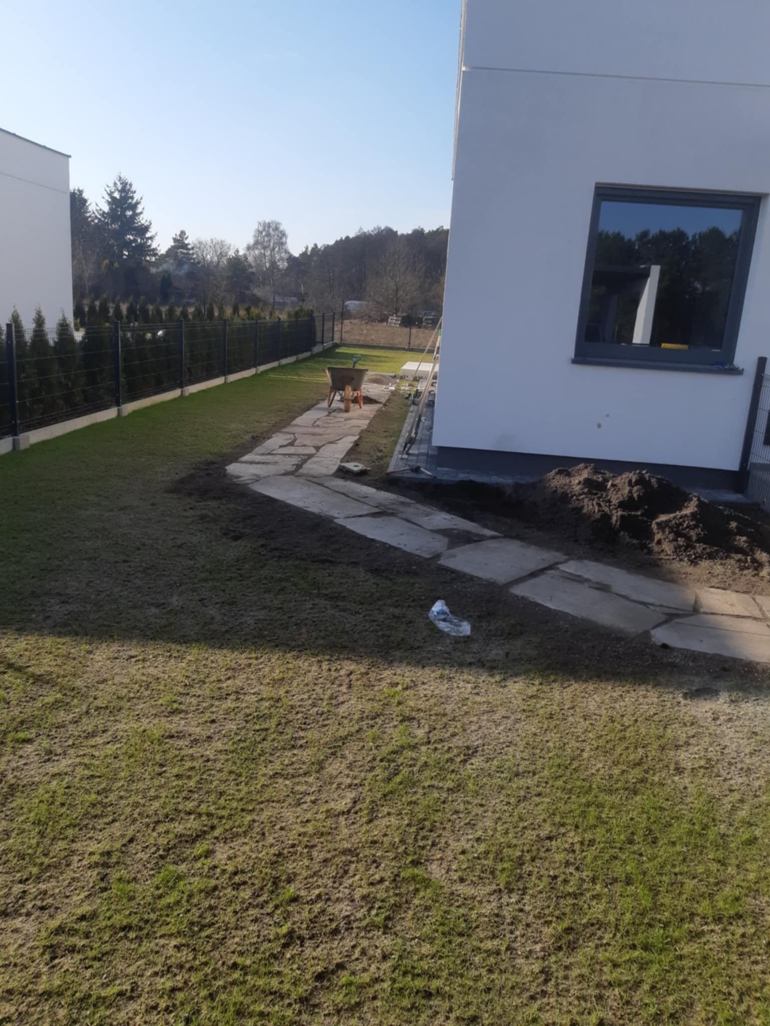 Prace ziemne w Białe Błota: wyrównywanie terenu pod trawnik, widoczna ścieżka z płyt kamiennych i taczka. Przygotowanie ogrodu do dalszych prac.