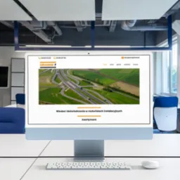 Monitor wyświetla stronę internetową orangeseven.pl z widokiem na autostradę z lotu ptaka, umieszczony na biurku w nowoczesnym biurze.