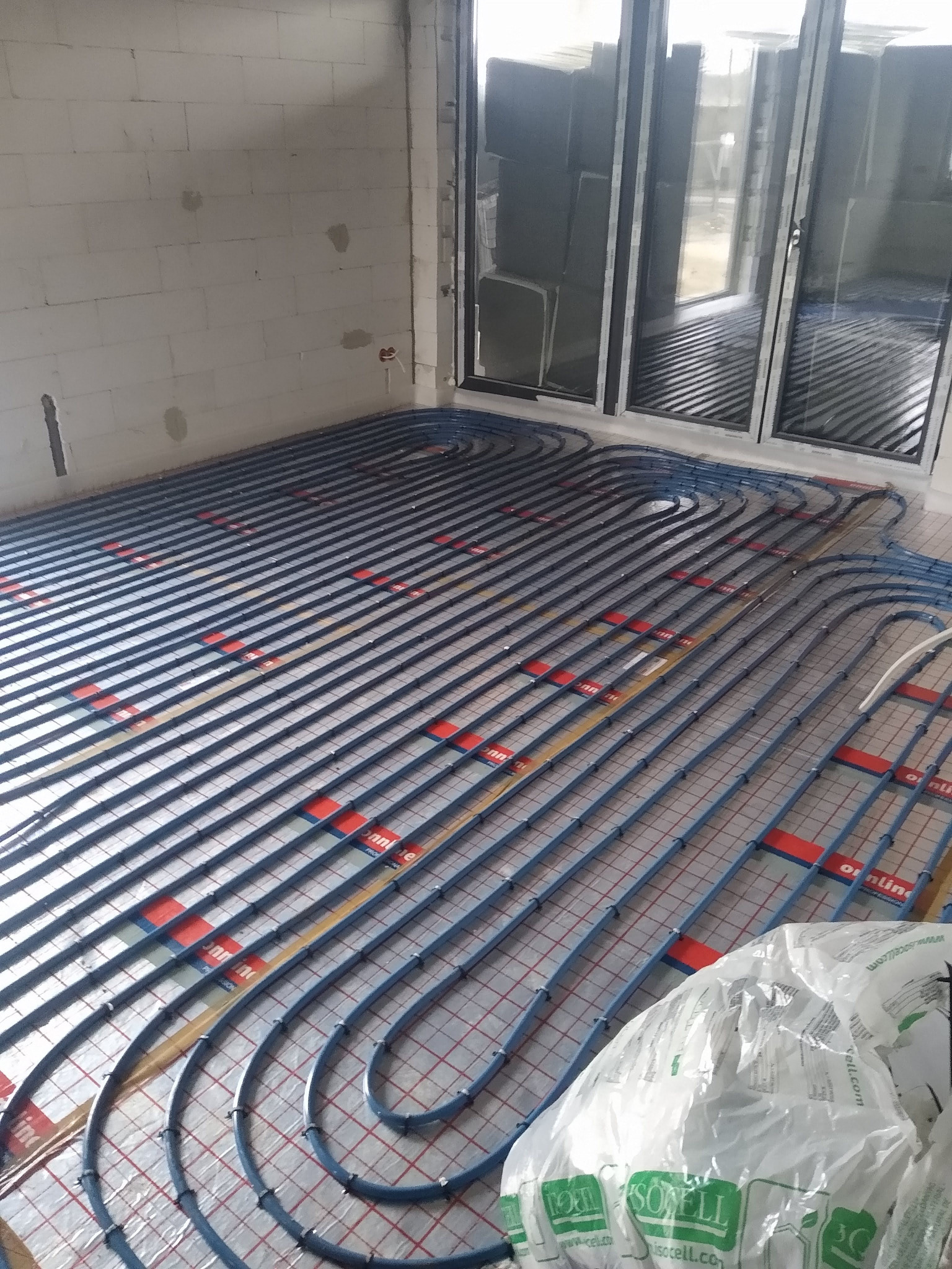 Instalacja ogrzewania podłogowego z rurami w kolorze niebieskim, zamocowanymi na folii z rastrem, widok z góry w Łasku. Stan surowy, przygotowanie do wylewki.