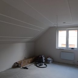SOLID Jakub Ragus - Pokój na poddaszu po szpachlowaniu i malowaniu, z dekoracyjnymi listwami na suficie i ścianach. Widoczne narzędzia i materiały malarskie.