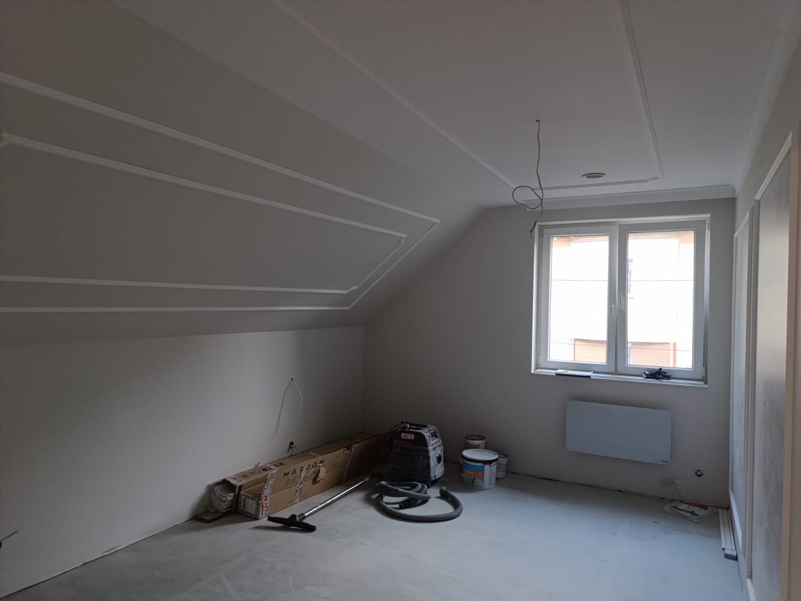 Pokój na poddaszu po szpachlowaniu i malowaniu, z dekoracyjnymi listwami na suficie i ścianach. Widoczne narzędzia i materiały malarskie.