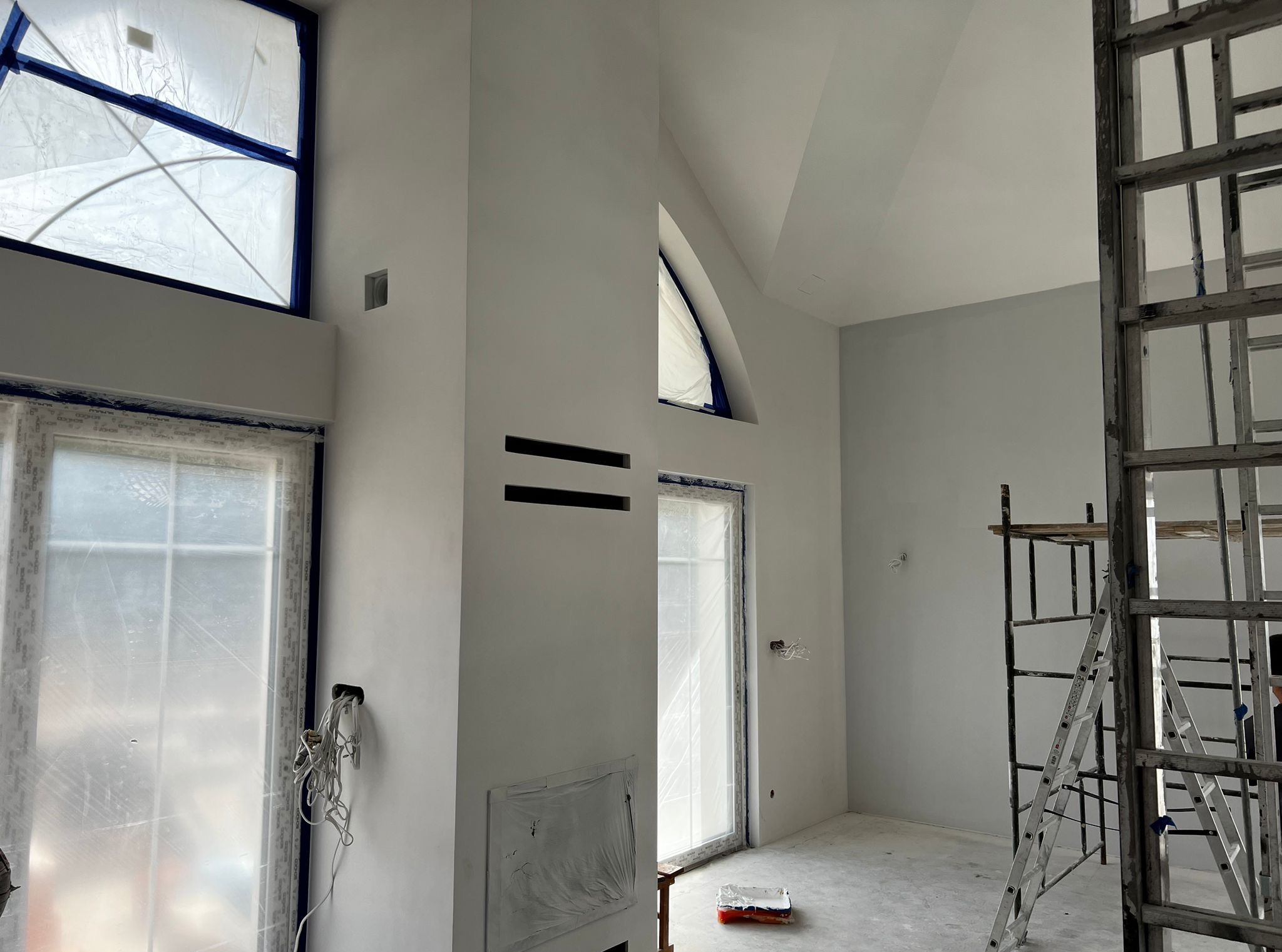Wnętrze po malowaniu w Żelechowie: ściany na biało, okna zabezpieczone folią, widoczne rusztowania. Minimalistyczny design z elementami surowego wykończenia.