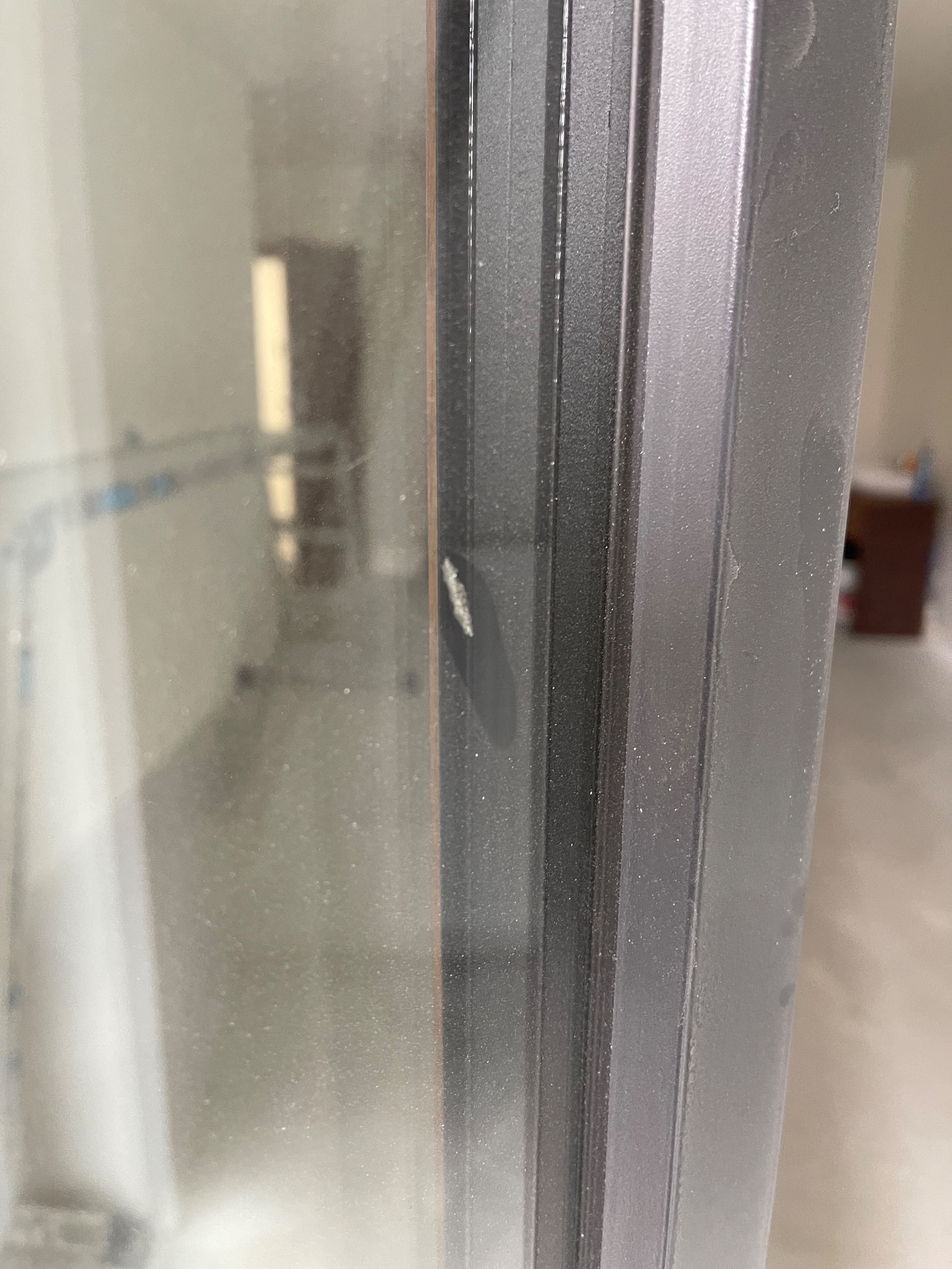 Szczegółowe ujęcie brudnej ramy okiennej z widocznymi smugami i kurzem na szybie, wnętrze mieszkania w tle.