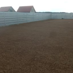 Grzegorz Rupacki ROLBUD - Przygotowany teren pod trawnik, wyrównana ziemia, otoczony białym, nowoczesnym ogrodzeniem panelowym. W tle widoczne budynki mieszkalne.